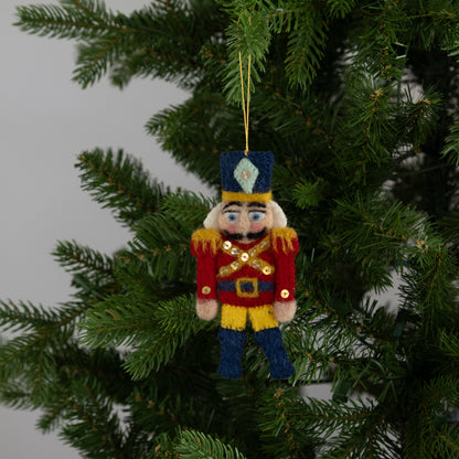 Felt ornament of a red and gold nutcracker hanging on a Christmas tree.