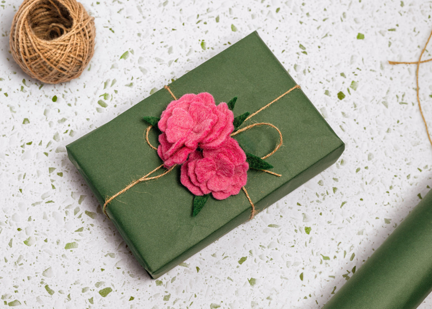 Felt pink carnation flower gift topper tied around green wrapped present.
