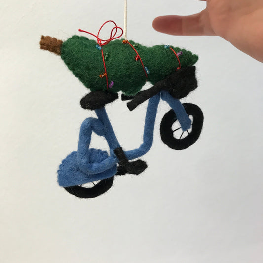 Felt ornament of a blue bike with a Christmas tree on top with a hand holding the string.