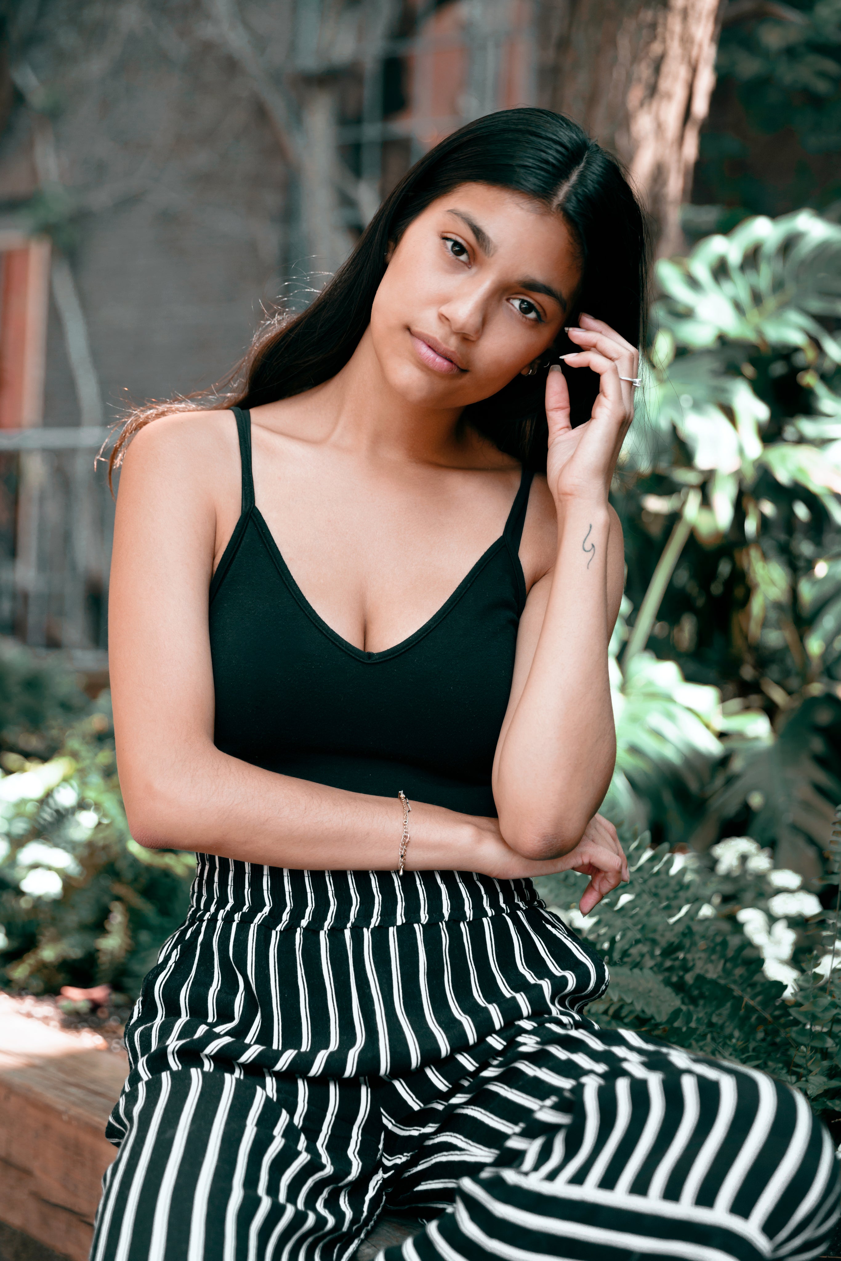 Woman with black spaghetti strap top and black and white striped pants sitting with hand brushing hair out of face.