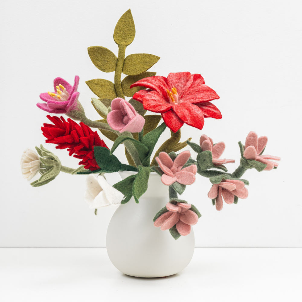 Bouquet of pink, red, and white felt flowers and green leaves in a white vase.