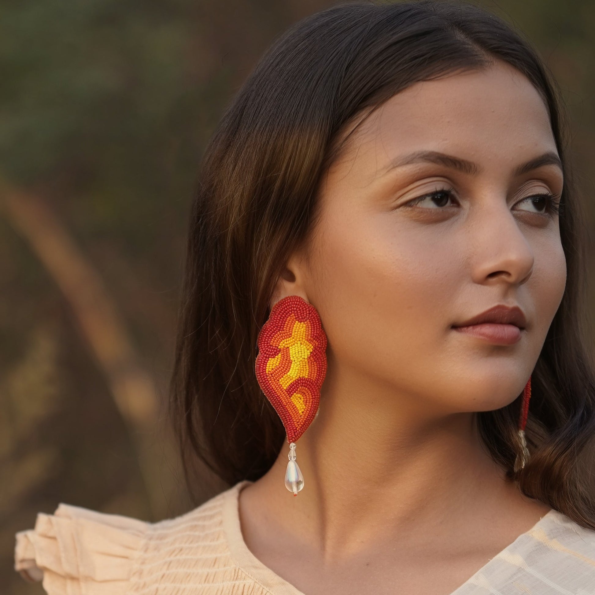 Right front view of woman wearing red, orange, yellow glass beaded earrings with clear drop bead.