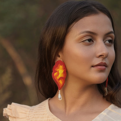 Right front view of woman wearing red, orange, yellow glass beaded earrings with clear drop bead.