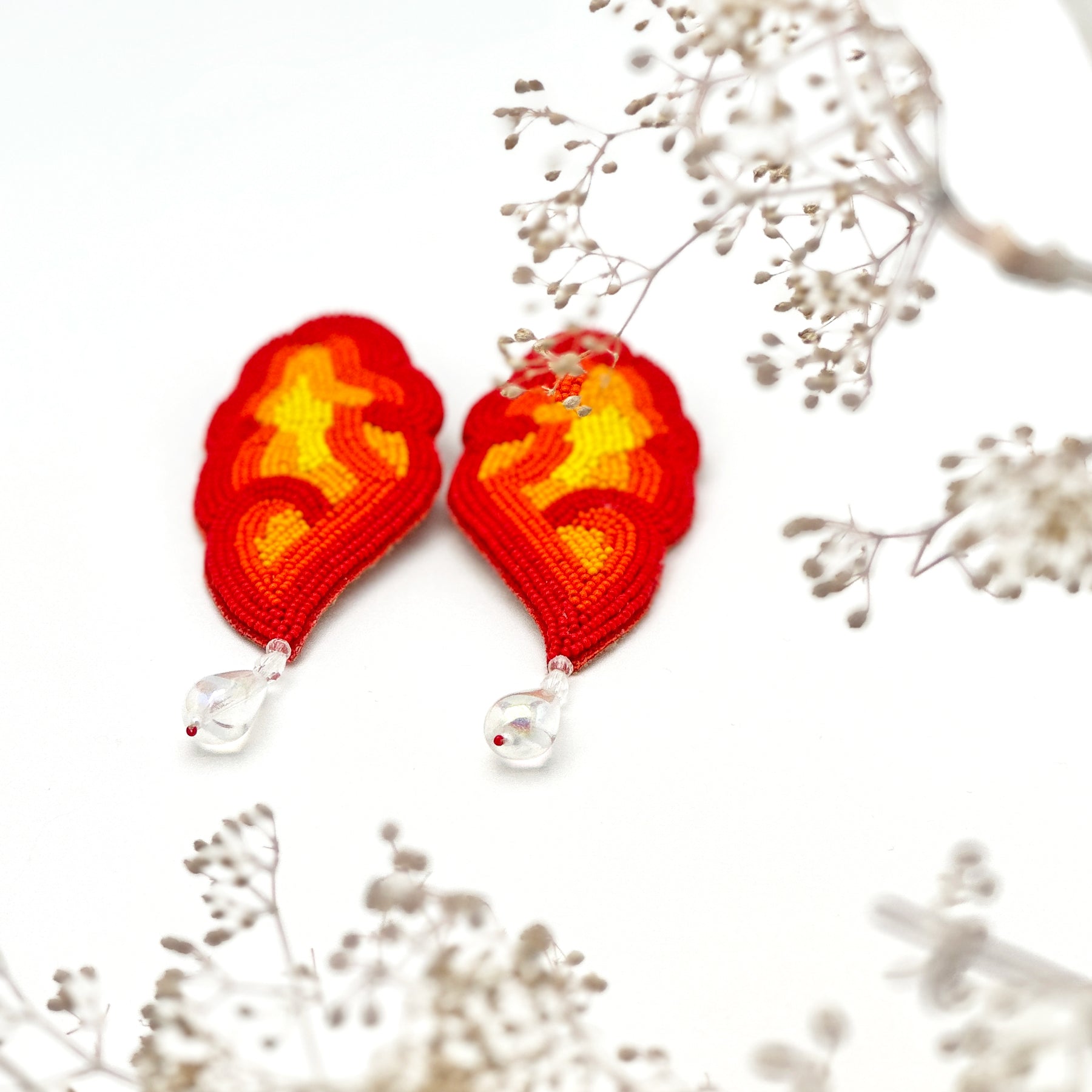 Pair of red, orange, yellow glass beaded earrings with clear drop bead on black and white background.