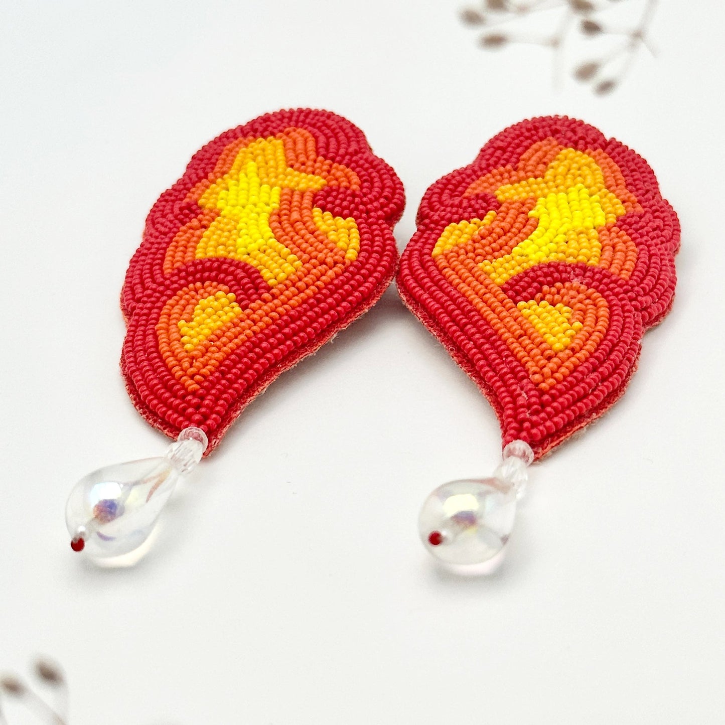 Closeup of red, orange, yellow glass beaded earrings with clear drop bead.
