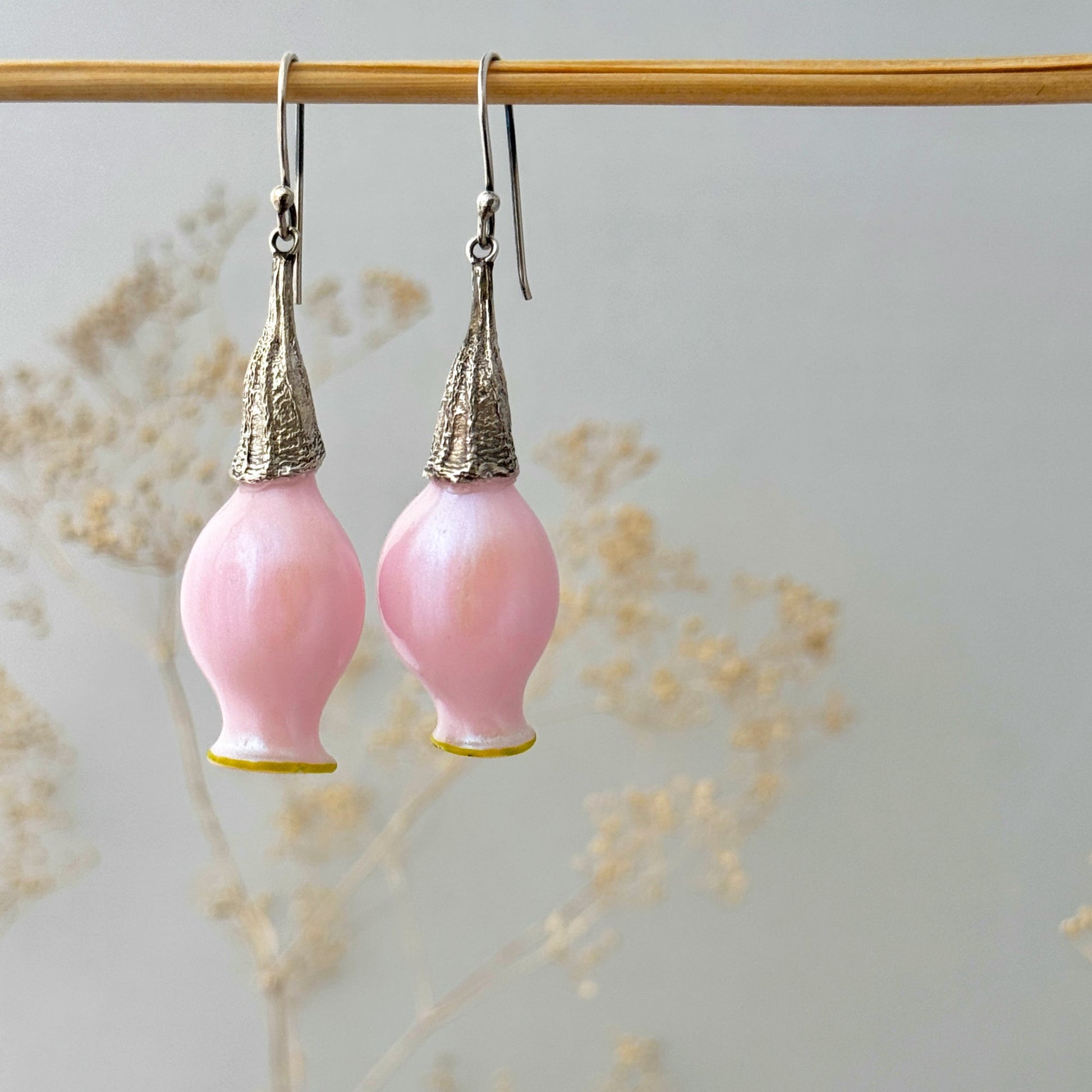 Pair of iridescent pink pod glass bud earrings with silver findings hanging from wood dowel.