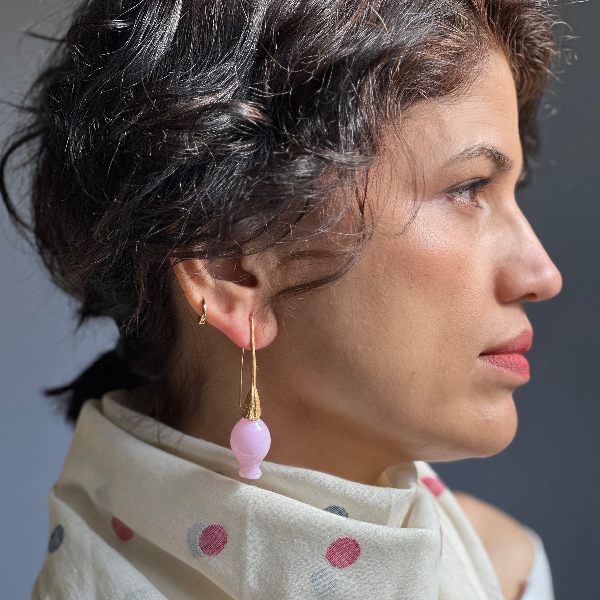 Right side view of woman wearing iridescent pink pod glass bud earrings with gold findings.