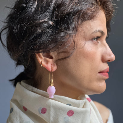 Right side view of woman wearing iridescent pink pod glass bud earrings with gold findings.