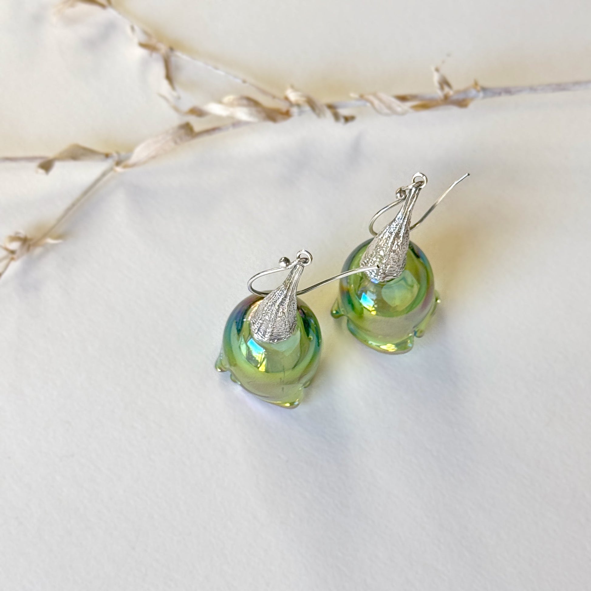 Pair of green pod glass earrings with silver findings standing upright.