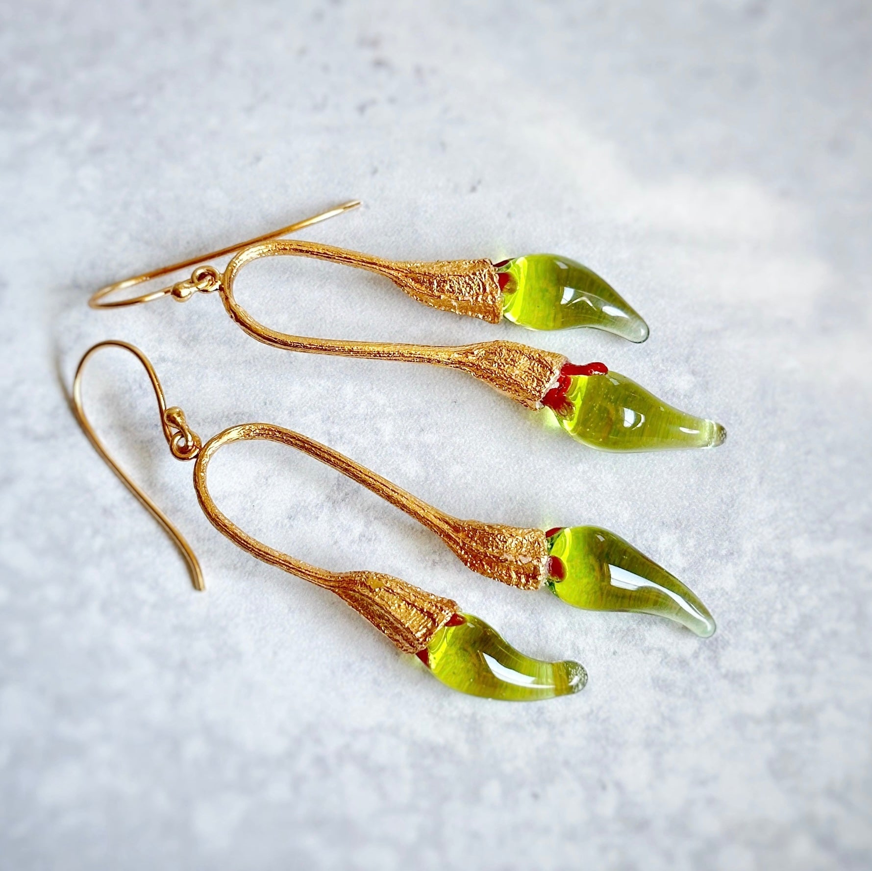 Pair of green and gold double chili pod earrings with silver colored findings.