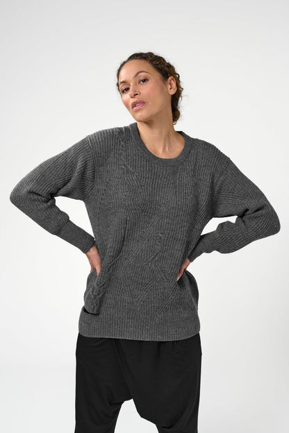 Woman with hands on waist wearing grey asymmetric crewneck sweater.