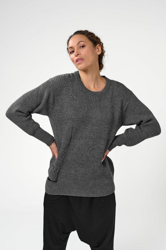 Woman with hands on waist wearing grey asymmetric crewneck sweater.