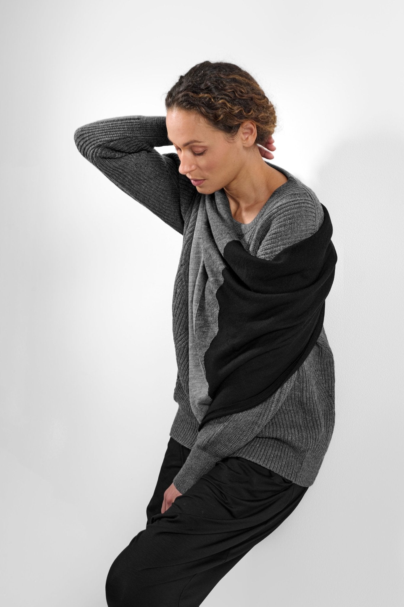 Side view of woman wearing grey sweater with black and grey modern Extrafine Merino wool scarf.