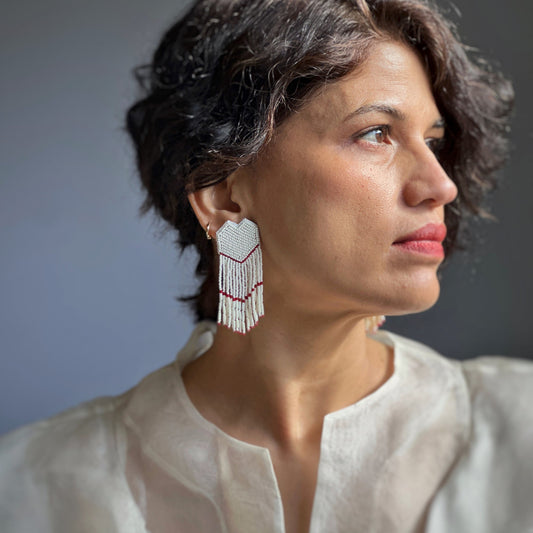 Right front view of woman wearing white and gold glass bead earrings with red accents.
