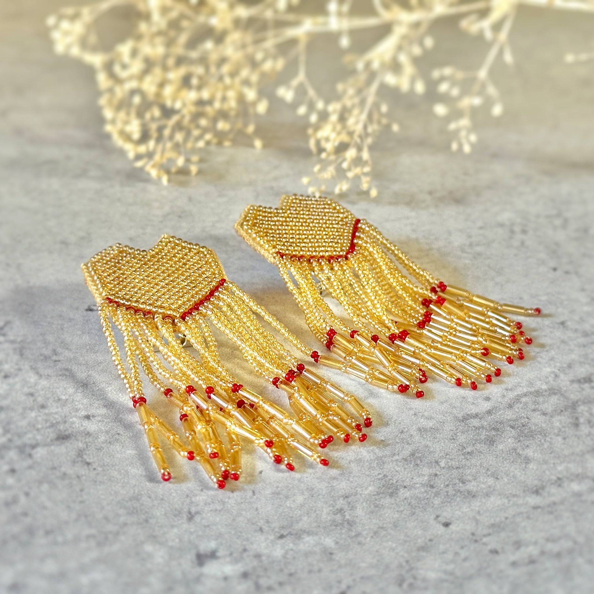 Pair of white and gold glass bead earrings with red accents on mottled grey background.  Small branch at top of image.
