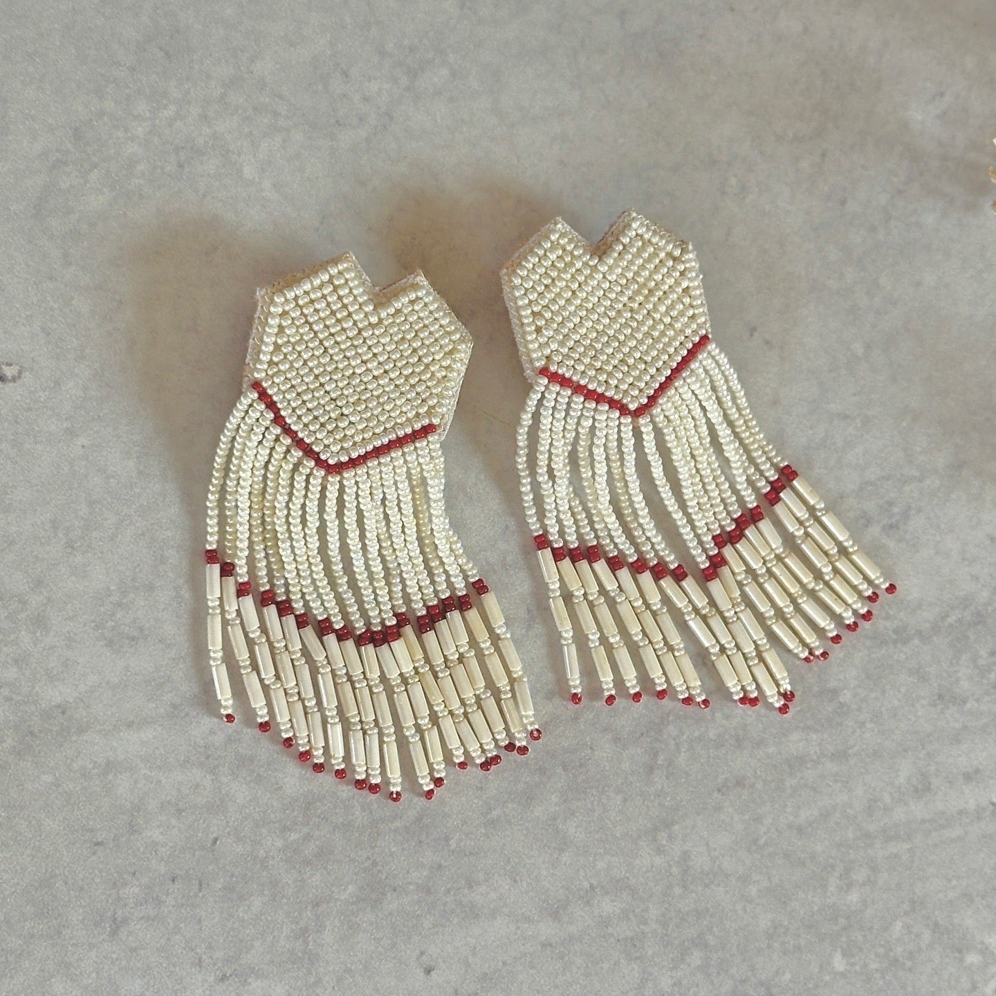 Pair of white and gold glass bead earrings with red accents on mottled grey background.