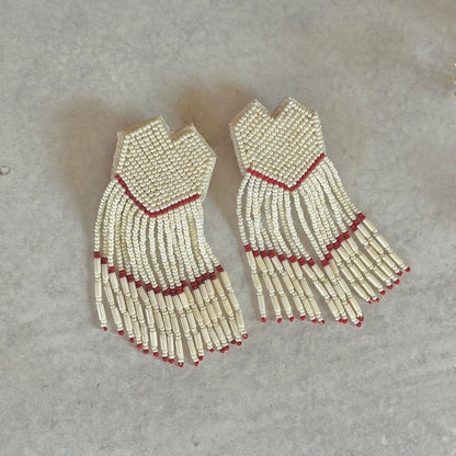 Pair of white and gold glass bead earrings with red accents on mottled grey background.