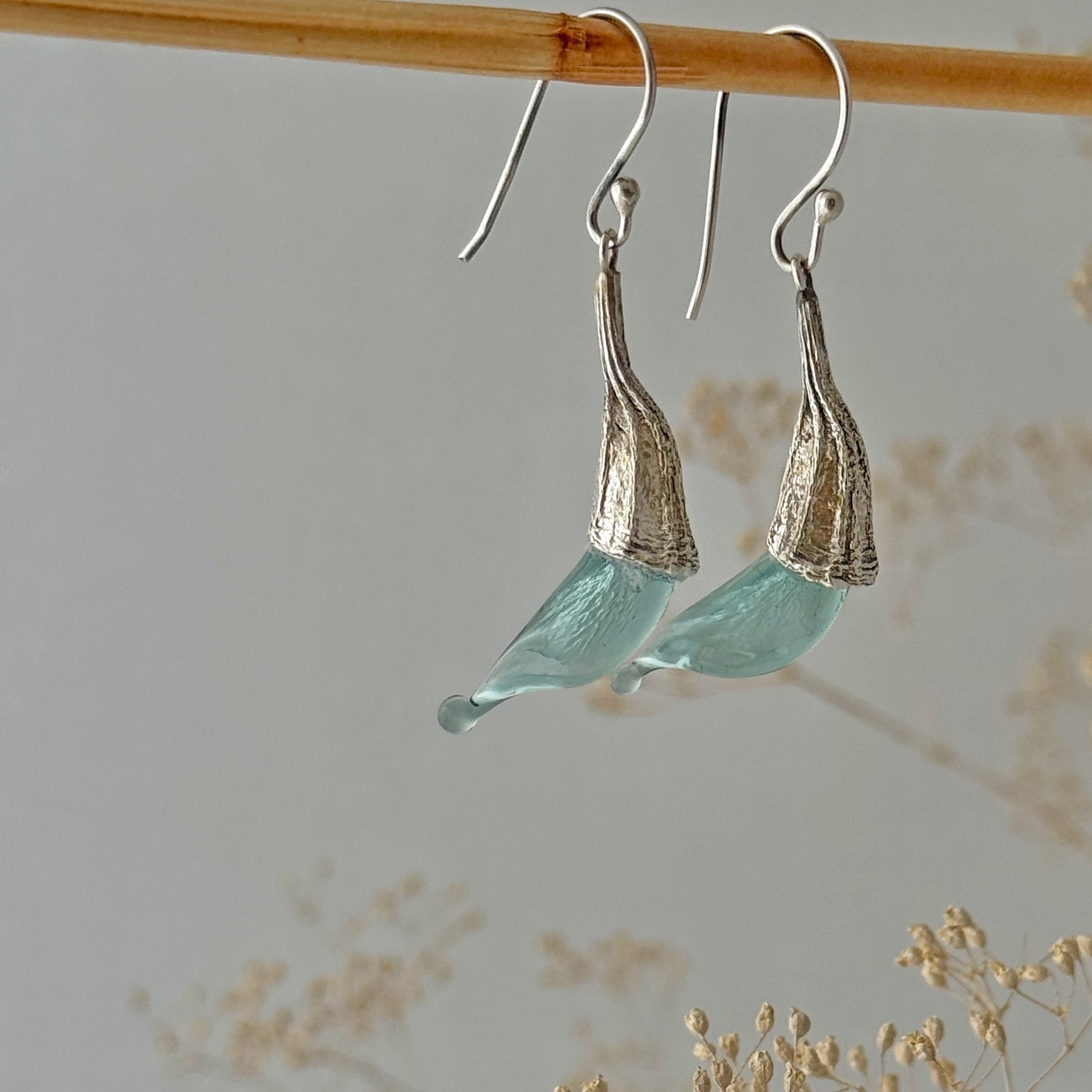 Pair of blue twisted glass petal earrings with silver findings hanging on wood dowel.