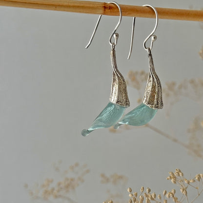 Pair of blue twisted glass petal earrings with silver findings hanging on wood dowel.