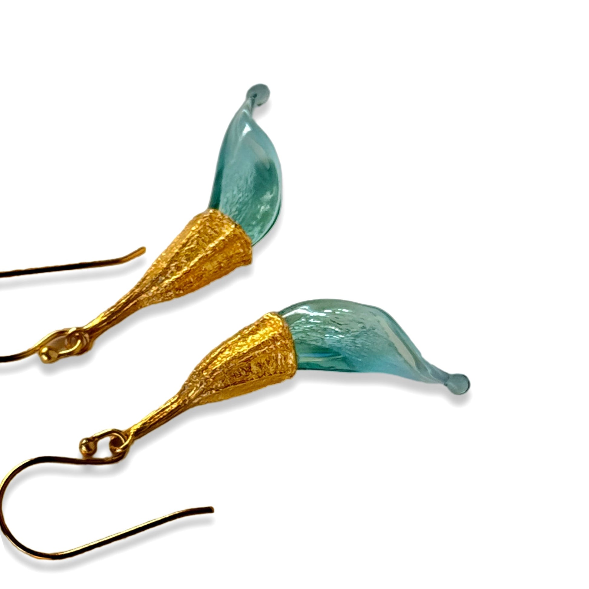 Pair of blue twisted glass petal earrings with gold findings laying on side.
