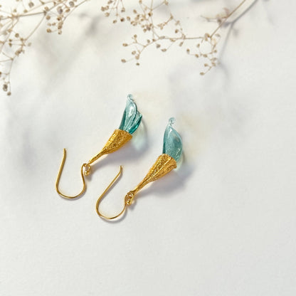 Pair of blue twisted glass petal earrings with gold findings upside down and dried flower twig above.