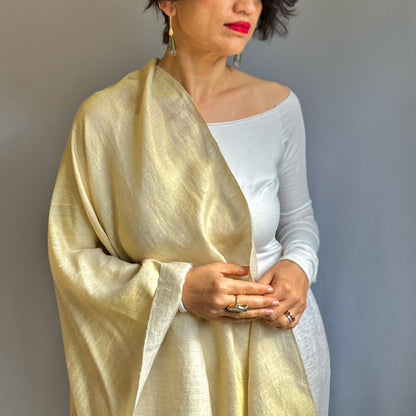 Woman in white dress with gold shimmering wrap draped over right shoulder.