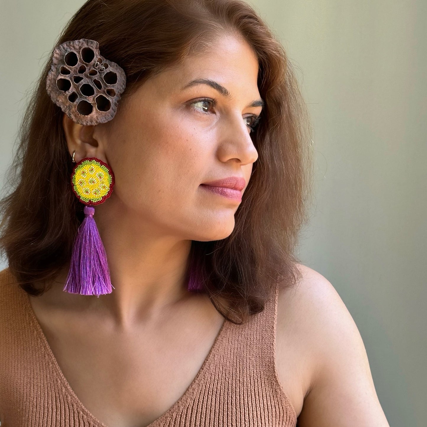 Right front view of woman wearing  yellow, green, purple beaded earrings with purple tassel.