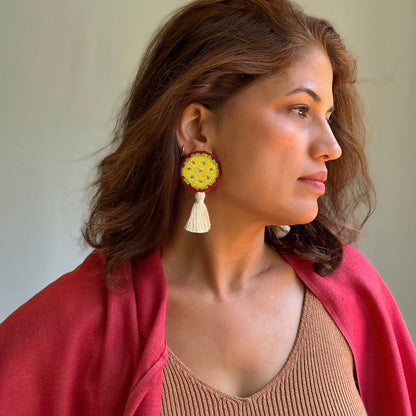 Right front view of woman wearing  yellow, green, purple beaded earrings with white tassel.