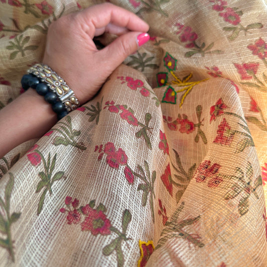 Closeup of woman's hand pinching material of a natural dye stole with pink, green, and yellow flowers.