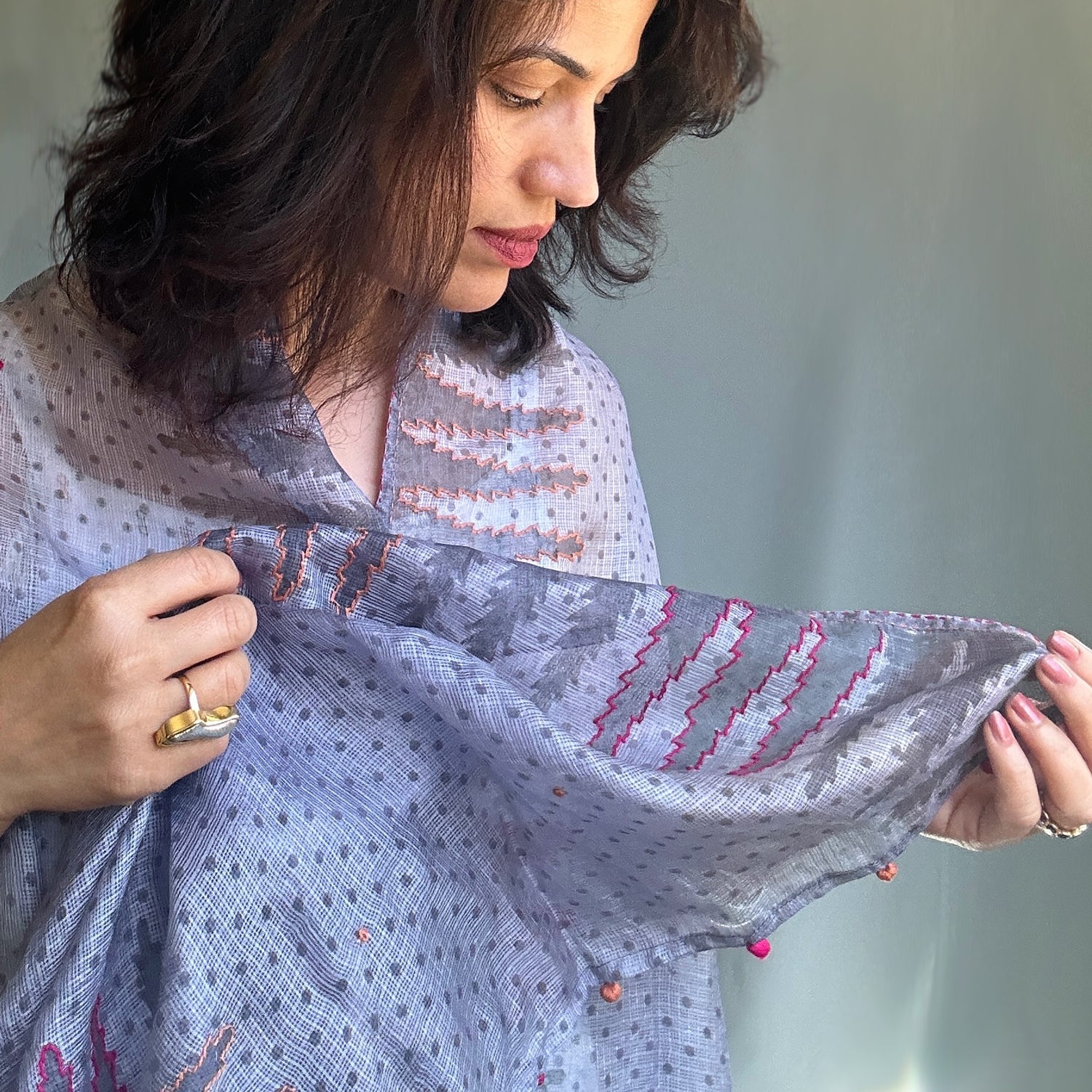 Woman wearing purplish grey scarf with tree motif, looking down at scarf and holding end in hand. Includes pink outlining.