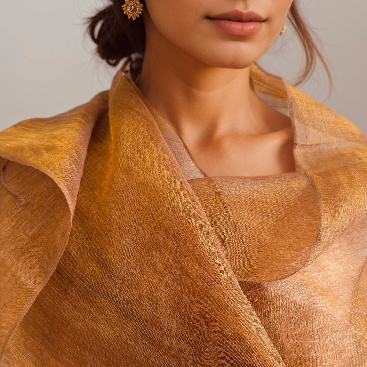 Rust orange handwoven linen scarf with gold zari metallic threads, dyed with natural myrobalan and tea, draped over a model’s shoulders.