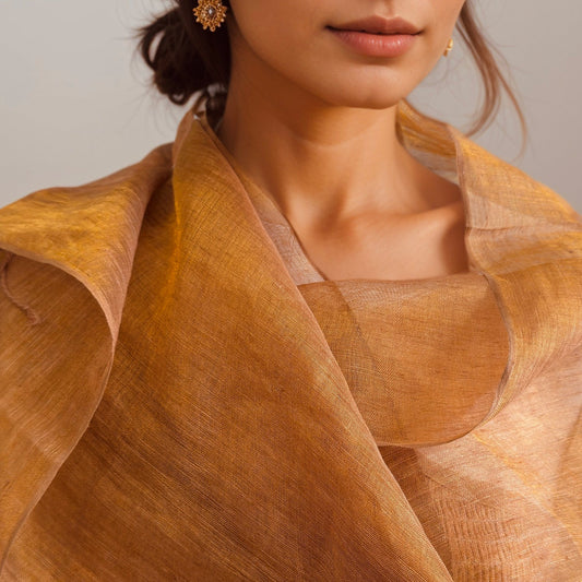 Rust orange handwoven linen scarf with gold zari metallic threads, dyed with natural myrobalan and tea, draped over a model’s shoulders.