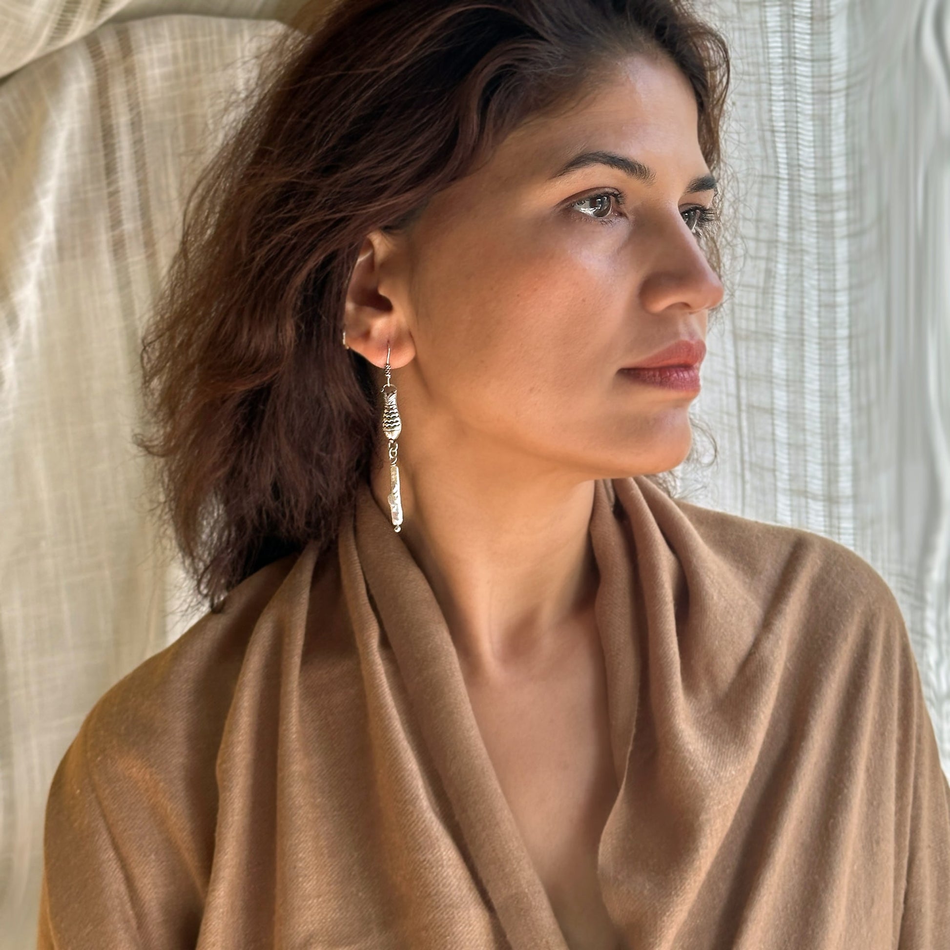 Right side view of woman wearing Silver and pearl dangle earings with fish motif.