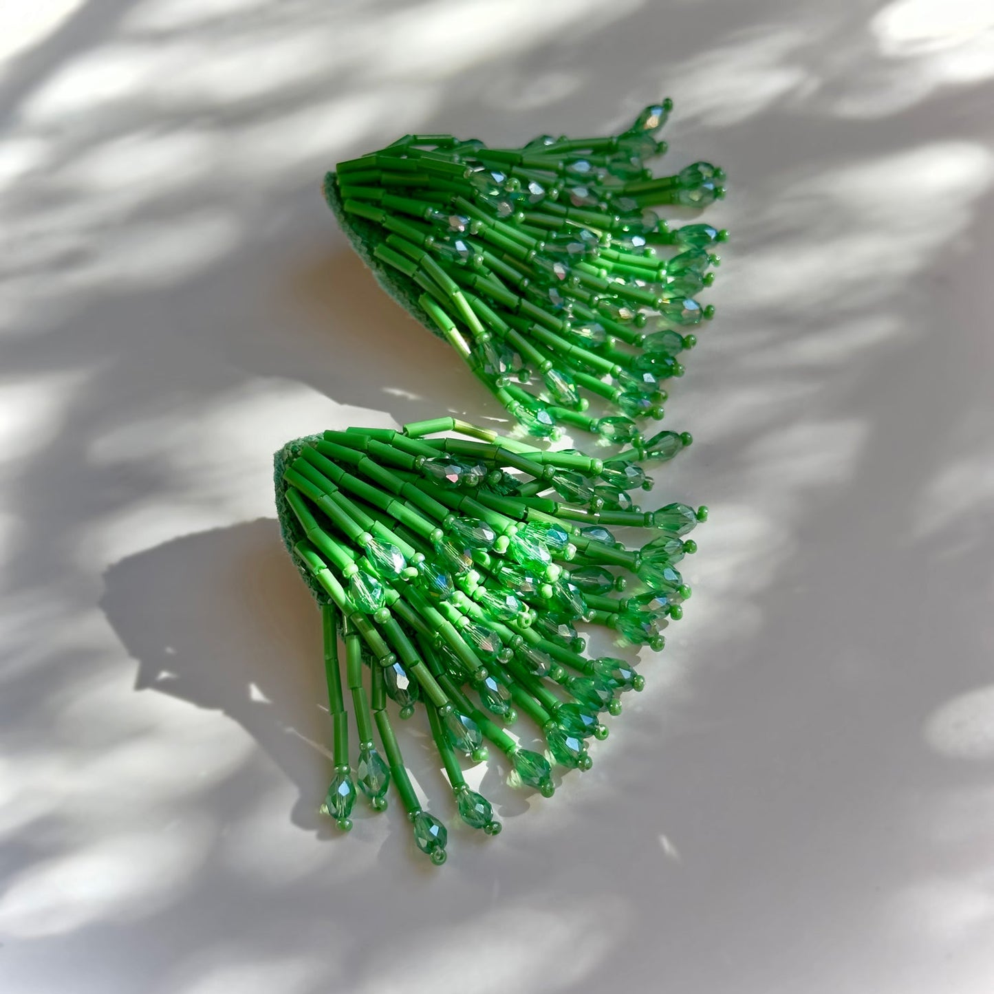 Pair of beaded green glass tassel earrings on shadowy background.