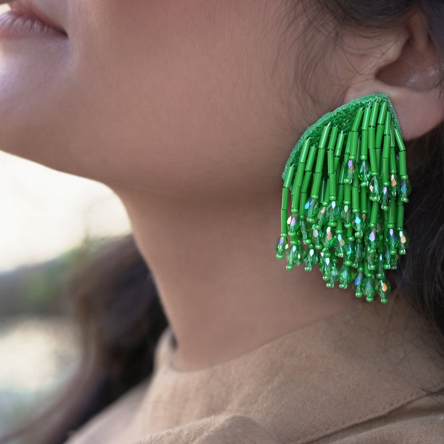 Closeup front left view of woman wearing beaded green glass tassel earrings.