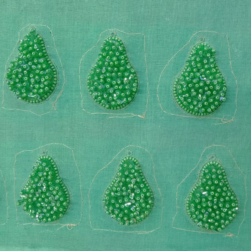 Six pincushion beaded green glass tassel earrings on green background.