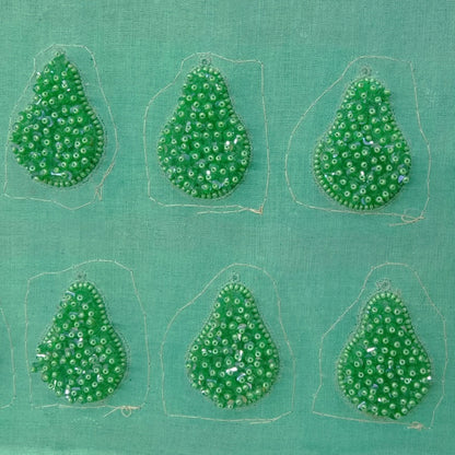 Six pincushion beaded green glass tassel earrings on green background.