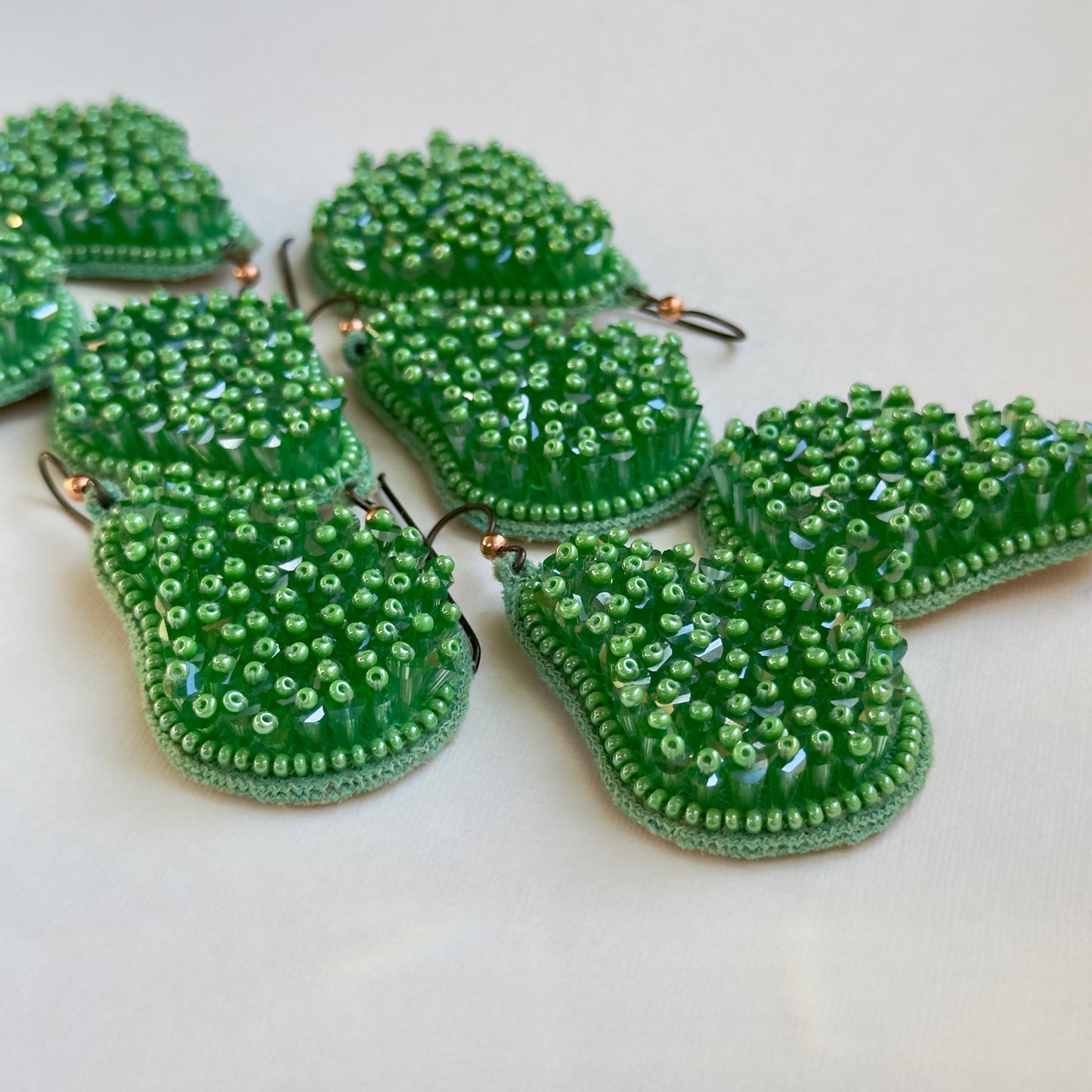 Many pincushion beaded green glass tassel earrings on grey background.