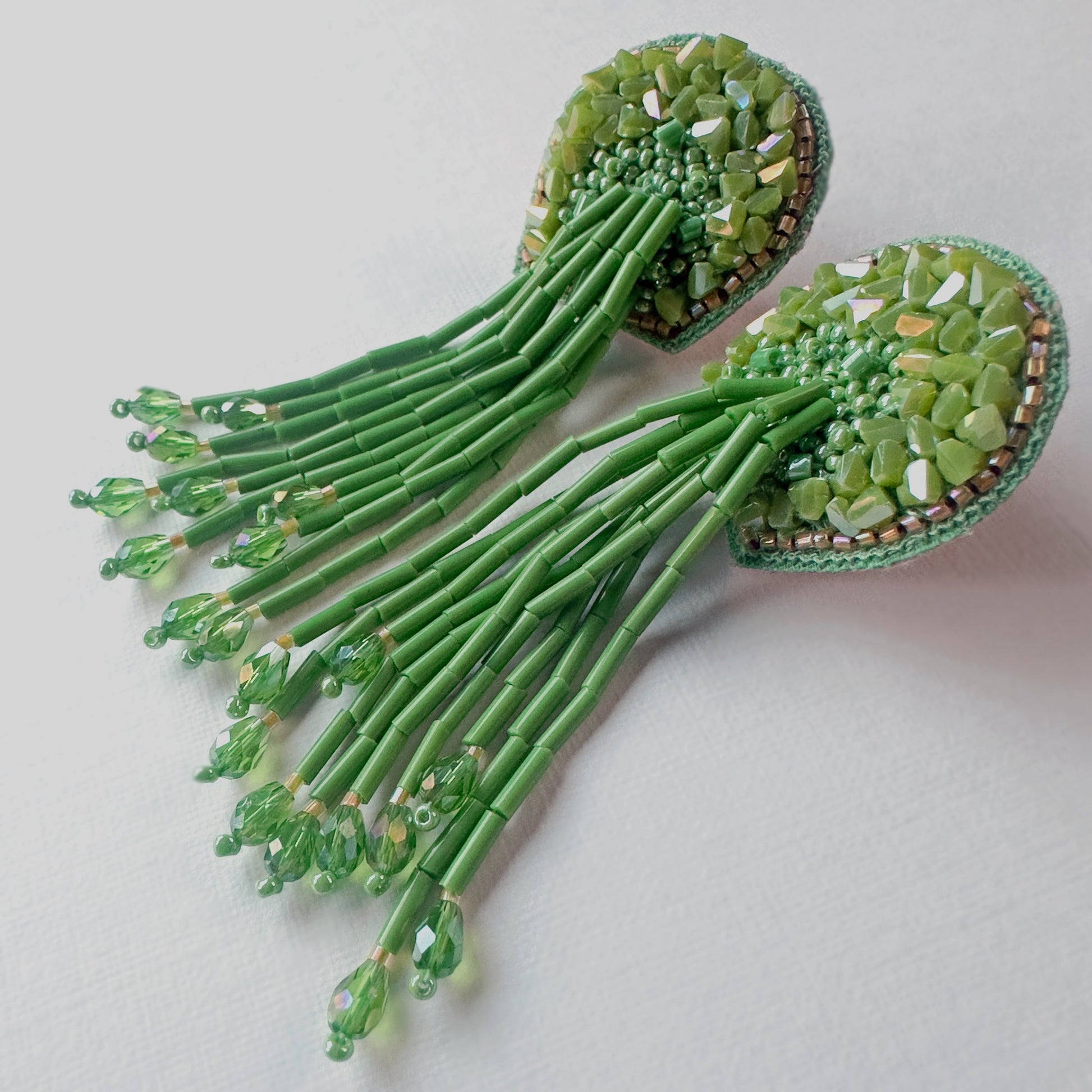 Pair of beaded green glass tassel earrings on grey background.