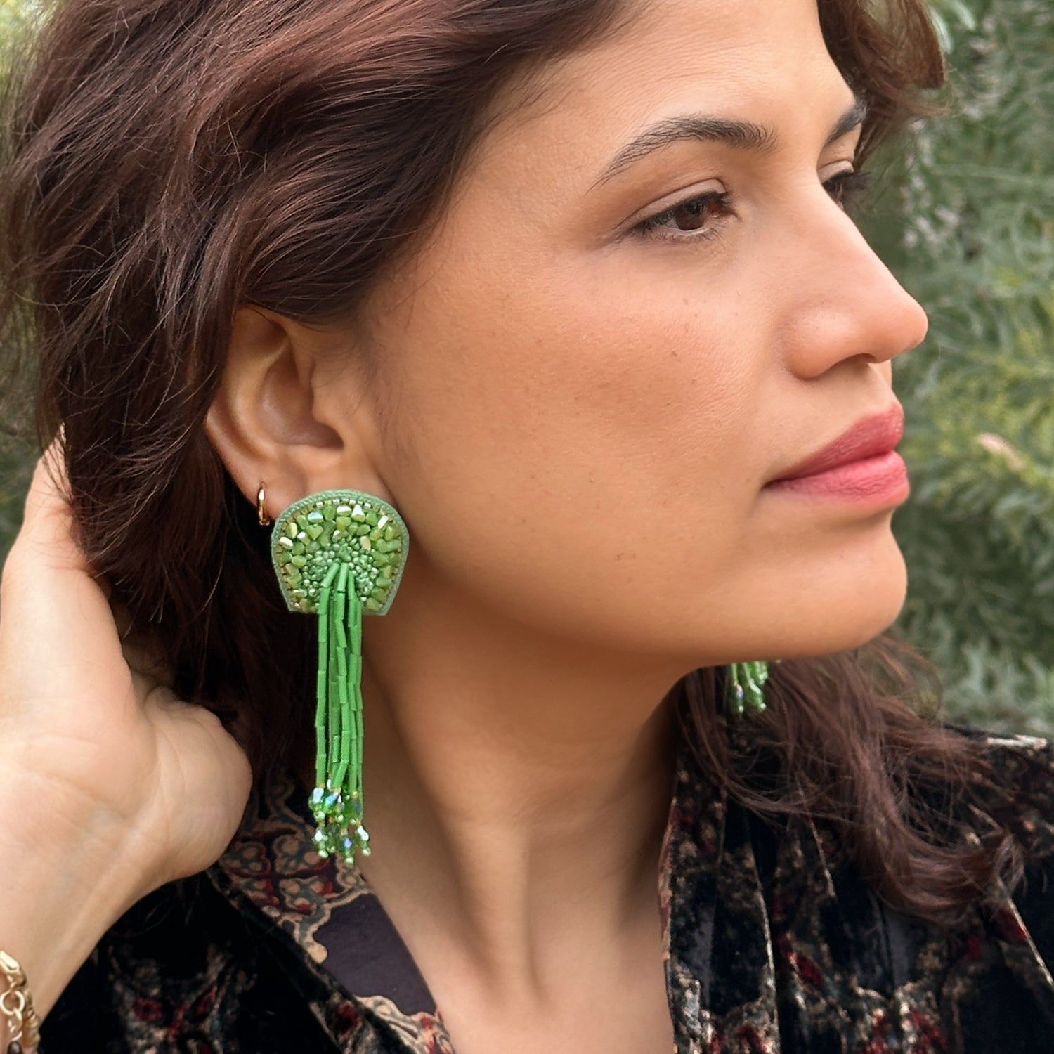Front right view of woman wearing  beaded green glass tassel earrings.