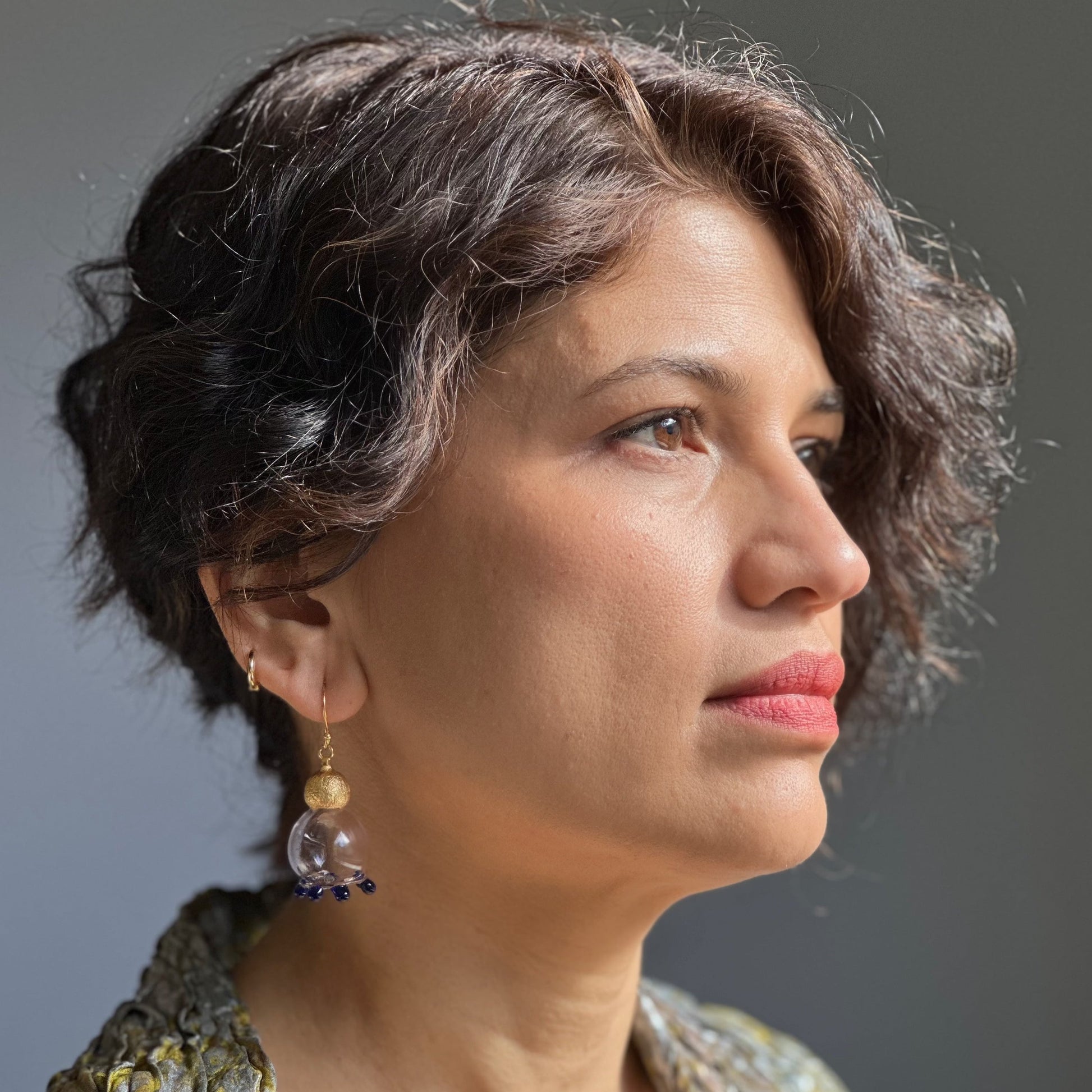 Right front view of woman wearing pale pink glass earrings with purple beads and gold plated findings.