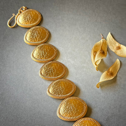 Gold bracelet with leaflet design in open vertical position on grey background.