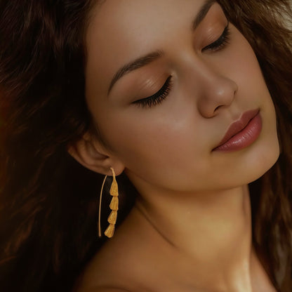 Front view of woman wearing gold plated dangle earrings.