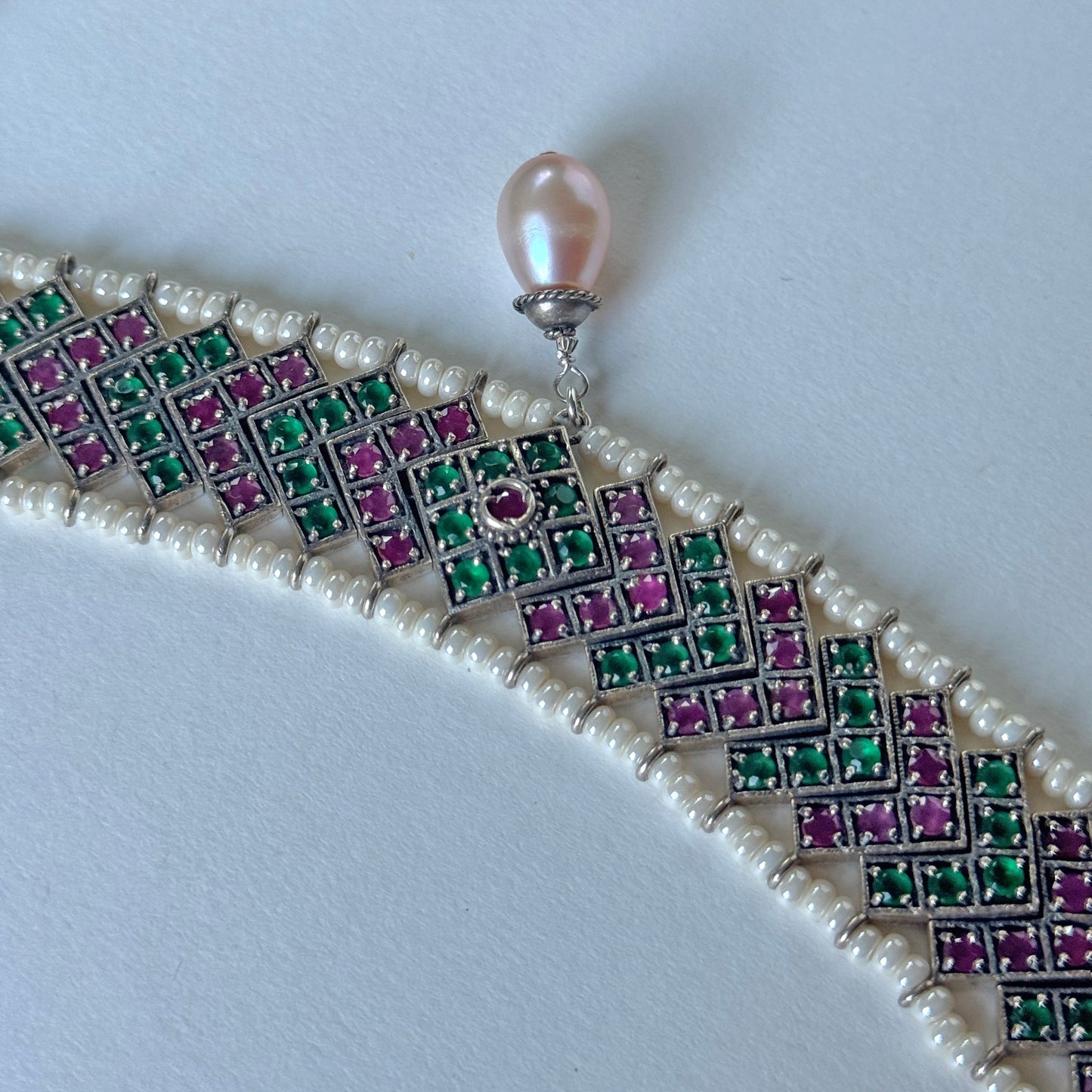 Green, red and silver choker necklace surrounded by white beads, with a drop pearl at the center.