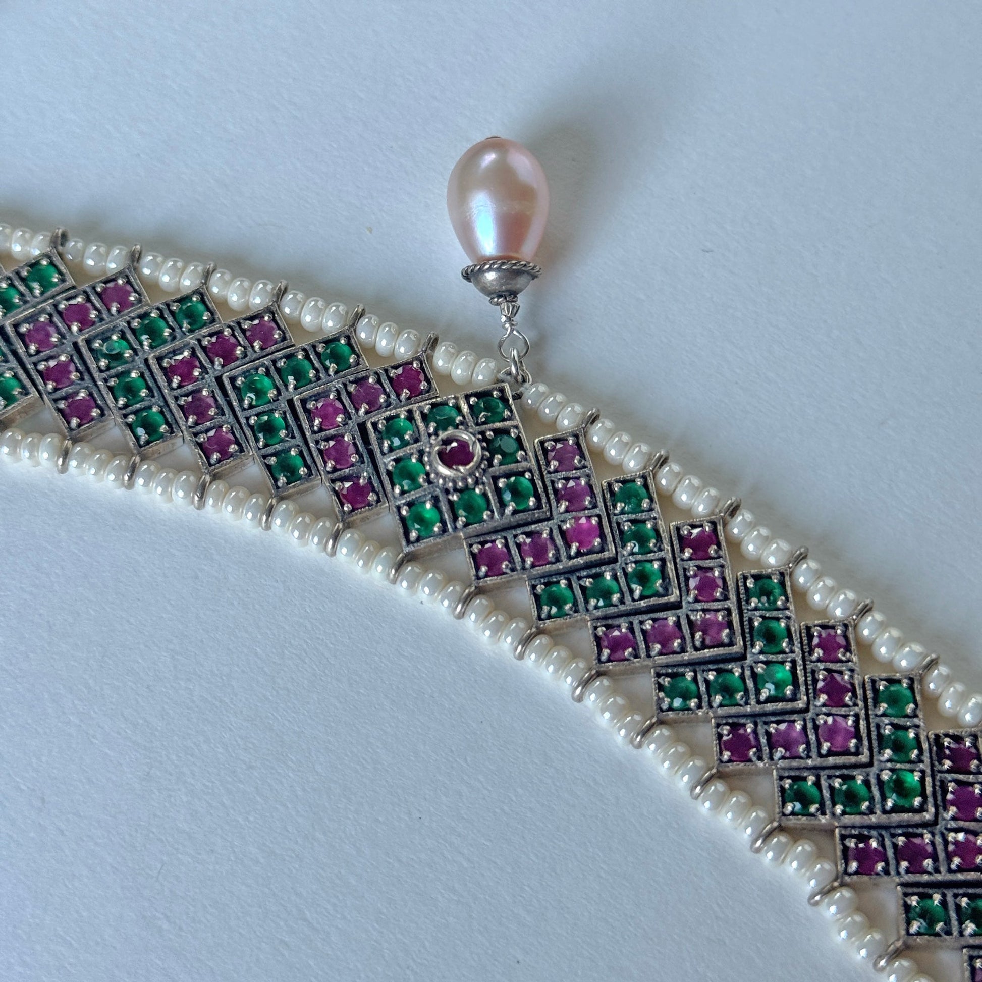Green, red and silver choker necklace surrounded by white beads, with a drop pearl at the center.