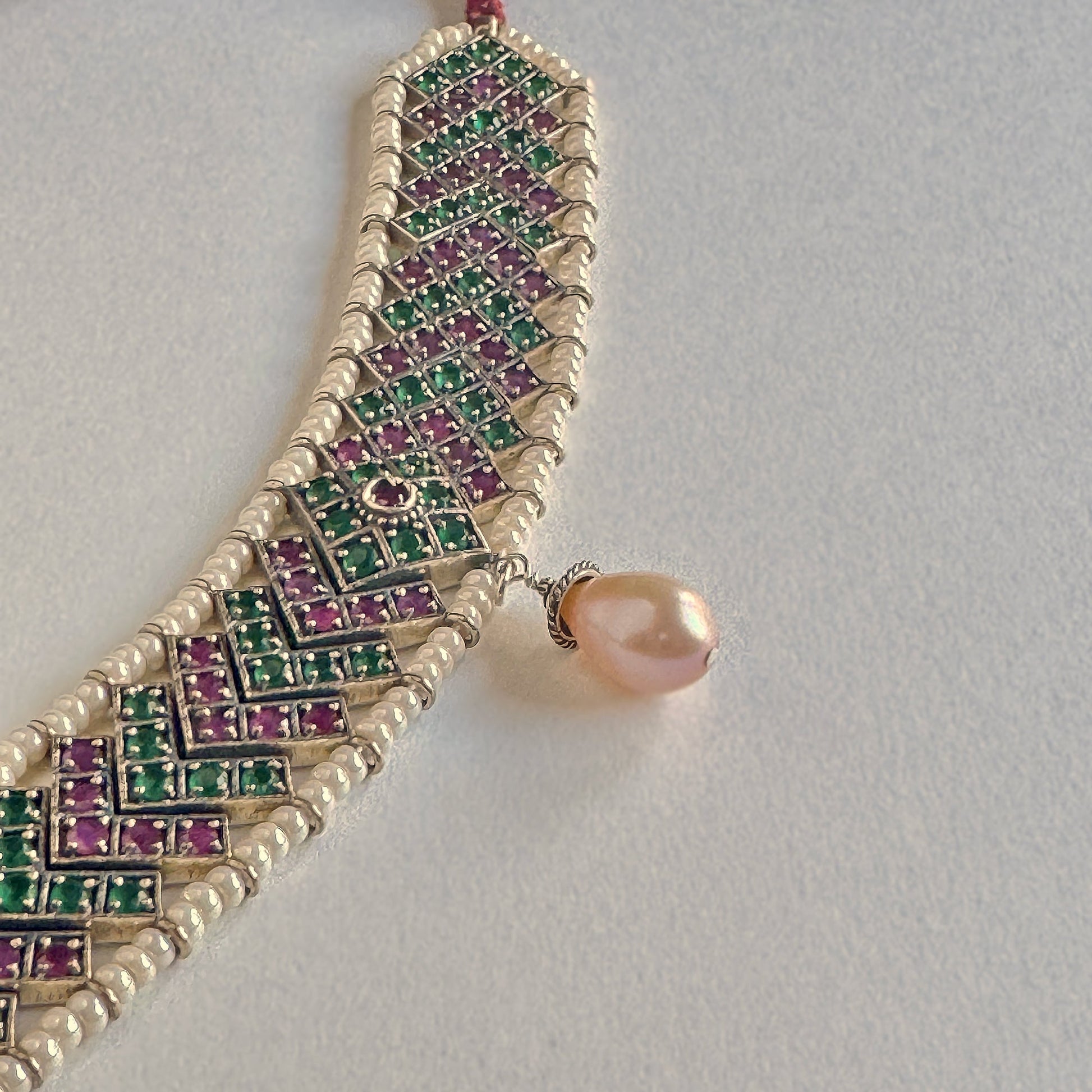 Green, red and silver choker necklace surrounded by white beads, with a drop pearl at the center.