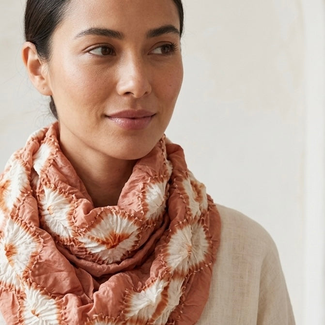 Natural sappanwood-dyed silk scarf in terracotta orange with white diamond shapes, draped around a model’s neck.