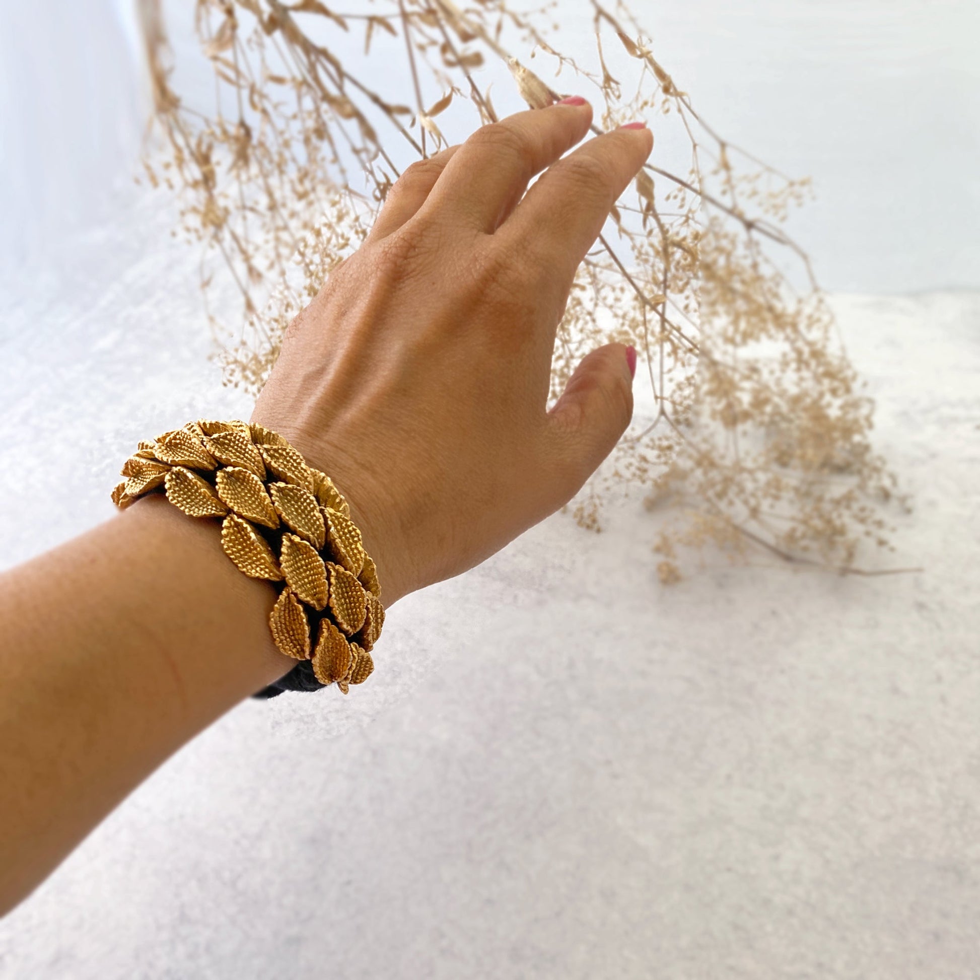 Woman's left hand wearing seedpod bracelet and touching dried flowers.