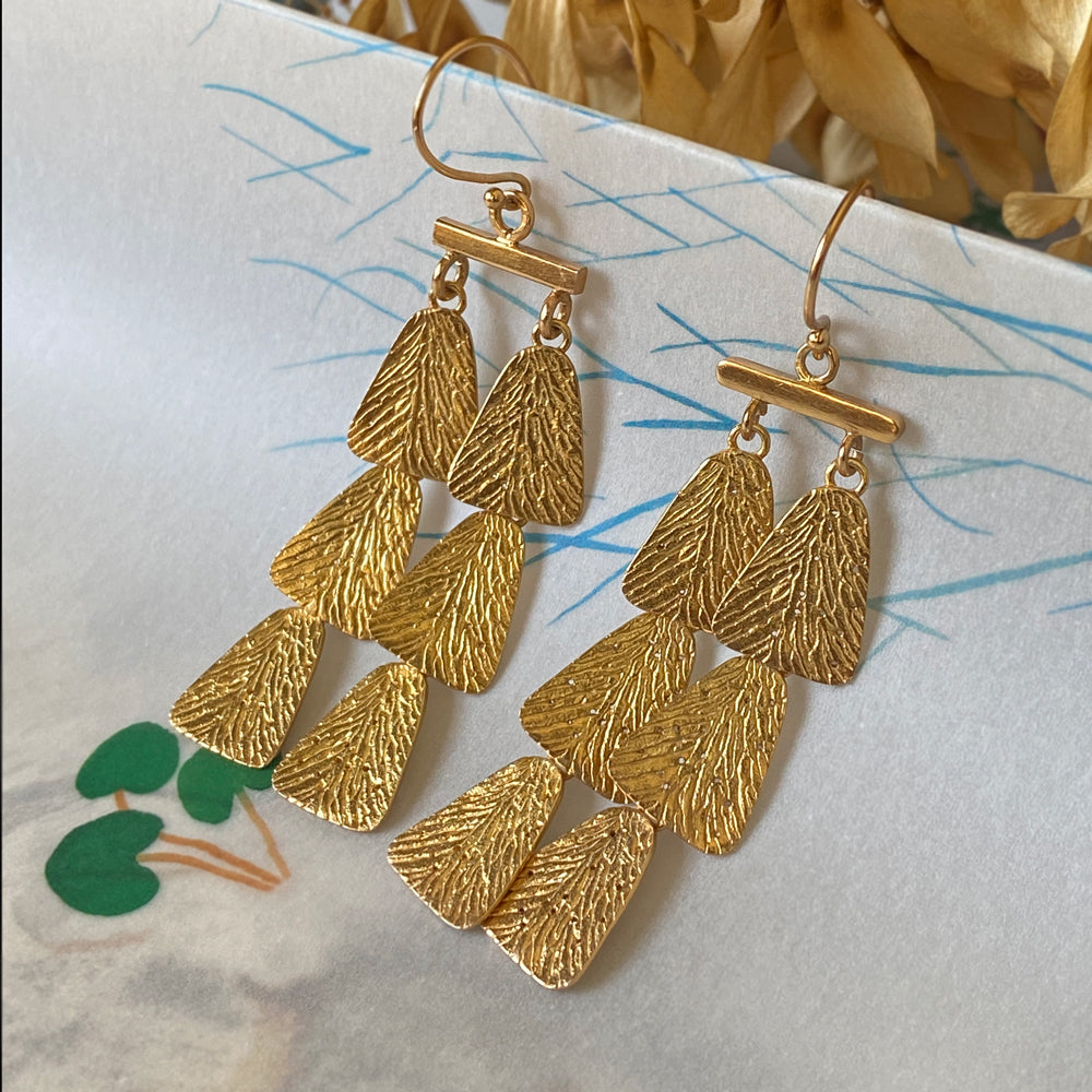 Pair of gold dangle earrings, each with 6 parts, on table.