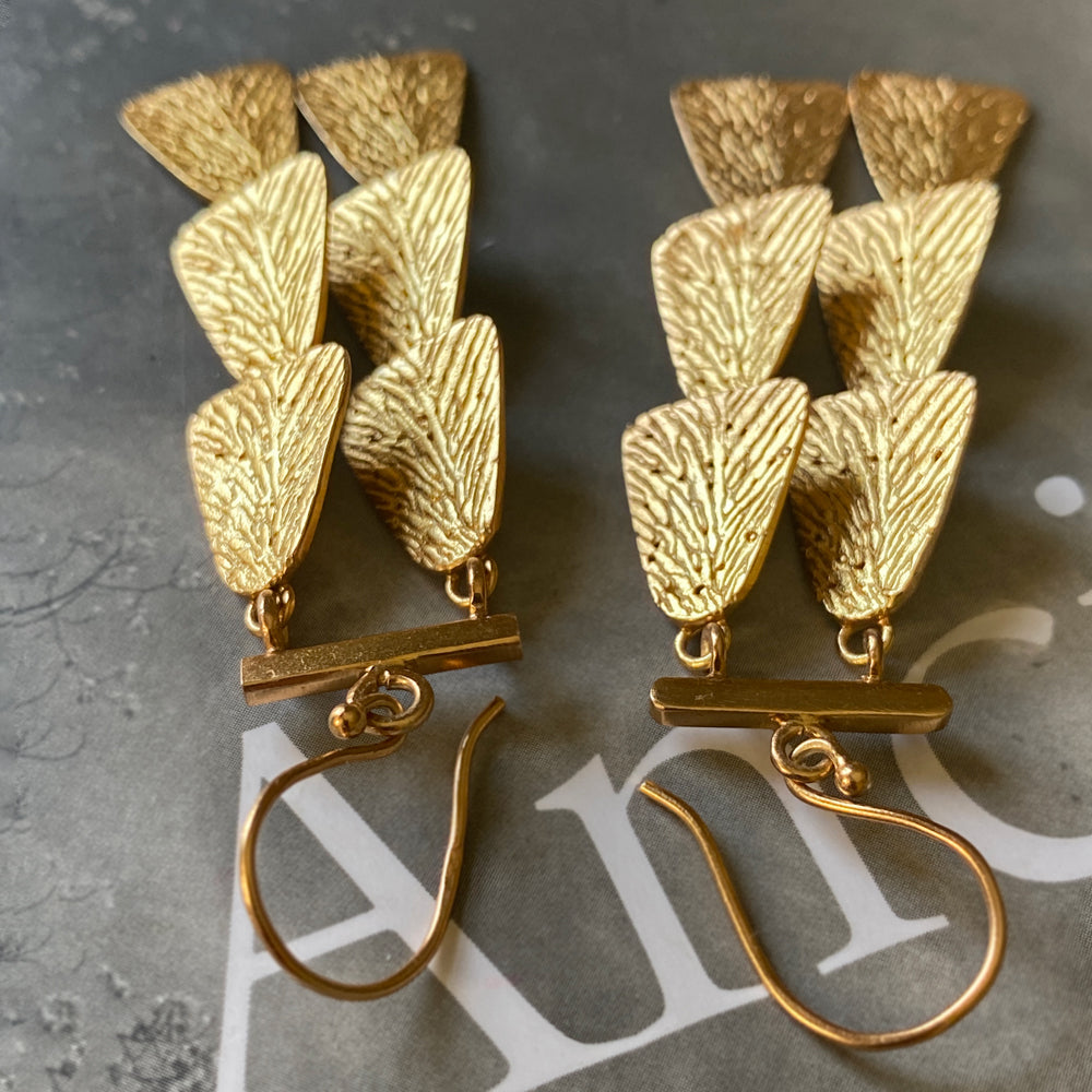 Pair of gold dangle earrings upside down on grey background.
